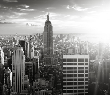 Black and white photo of New York City's Empire State Building with the sun shining behind it. 