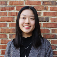 Headshot of 2020-21 Cutler-Bell Winner Emily Yuan. She is a young eastern asian woman with light skin, medium-length straight black hair, and a plaid grey suit jacket. She smiles against a brick wall.