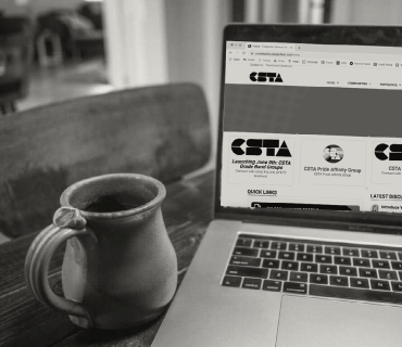 A black and white image of a laptop and a coffee mug. The laptop screen is opened to the CSTA homepage. 