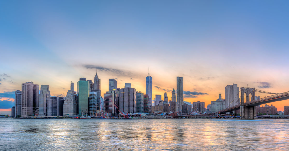 photo of the NYC skyline with the sun setting behind it and the hudson river in the foreground