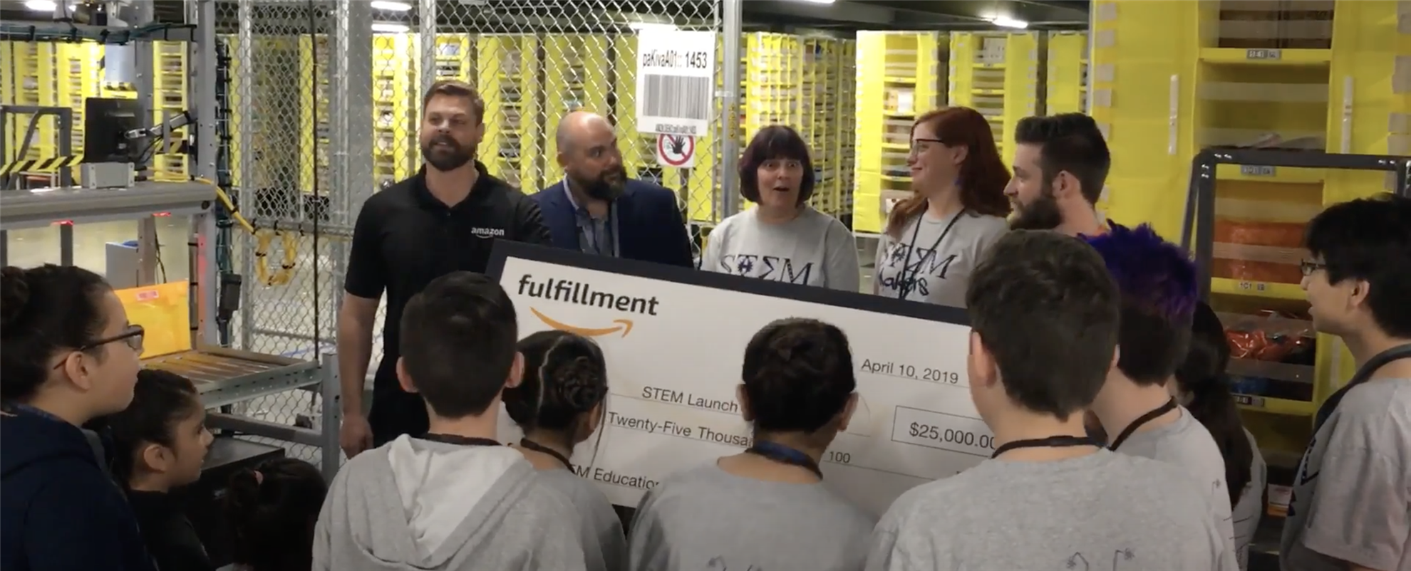 Students are gathered around as Amazon representatives surprise Deb Harding and other teachers with a giant $25,000 check