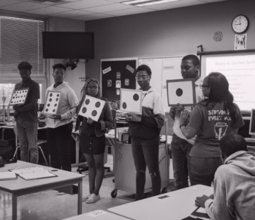 students holding up paper representing different sides of a die