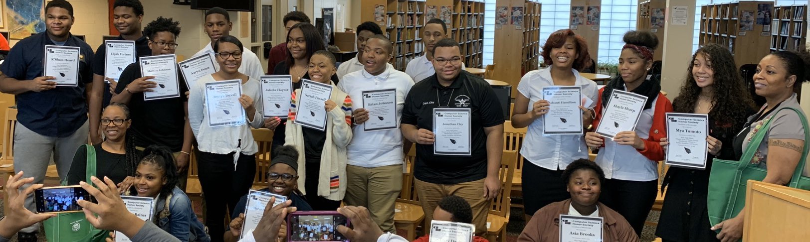 A class of black students in a library all holding up certificates of achievement - evidence of the success of being a warm demander