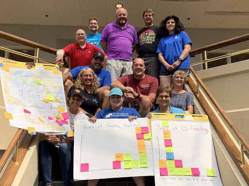 A group of Wisconsin CS teachers pose for a photo during summer professional development for the PUMP_CS project. Teachers hold signs indicating a high level of teaching experience and lower level of CS teaching experience.