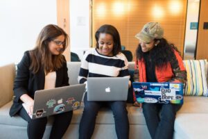 Three women with laptops sit together on a couch. 