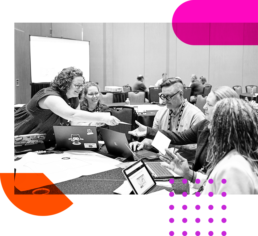 A smiling group sitting at a table at CSTA 2024. Two people reach across the others to exchange notecards. 