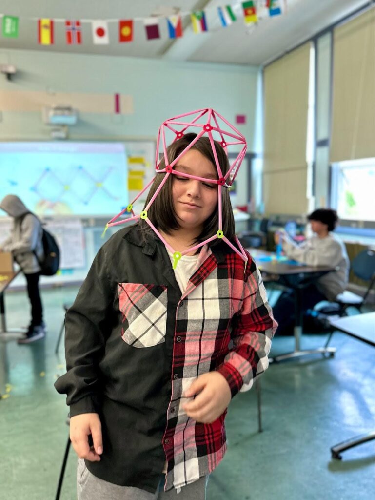 A student with a straw construction over their head, like an alien helmet