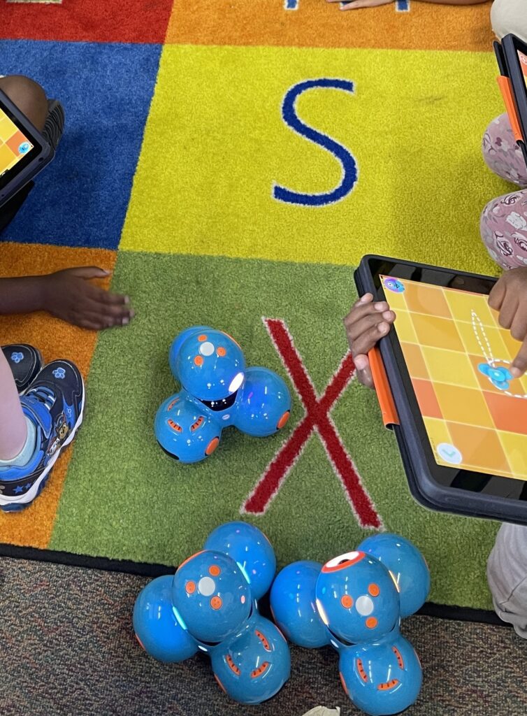 Elementary students using a tablet to give commands to the dash robots on the carpet