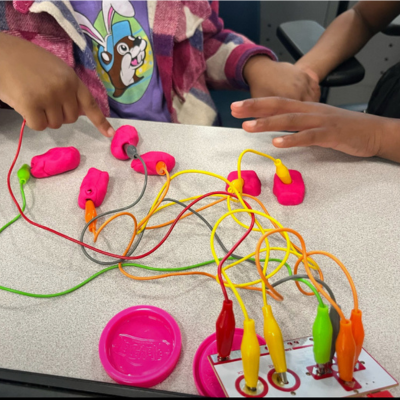 Students using a Makey Makey kit to create a soundboard out of PlayDoh.