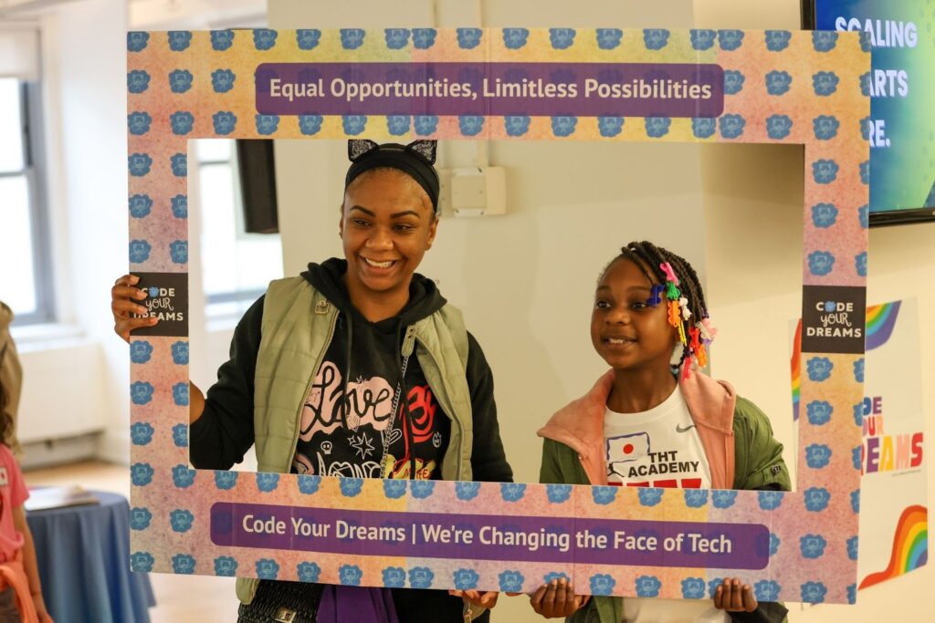 Students posing within a Code Your Dreams cut-out picture frame that reads "Equal opportunities, limitless possibilities."