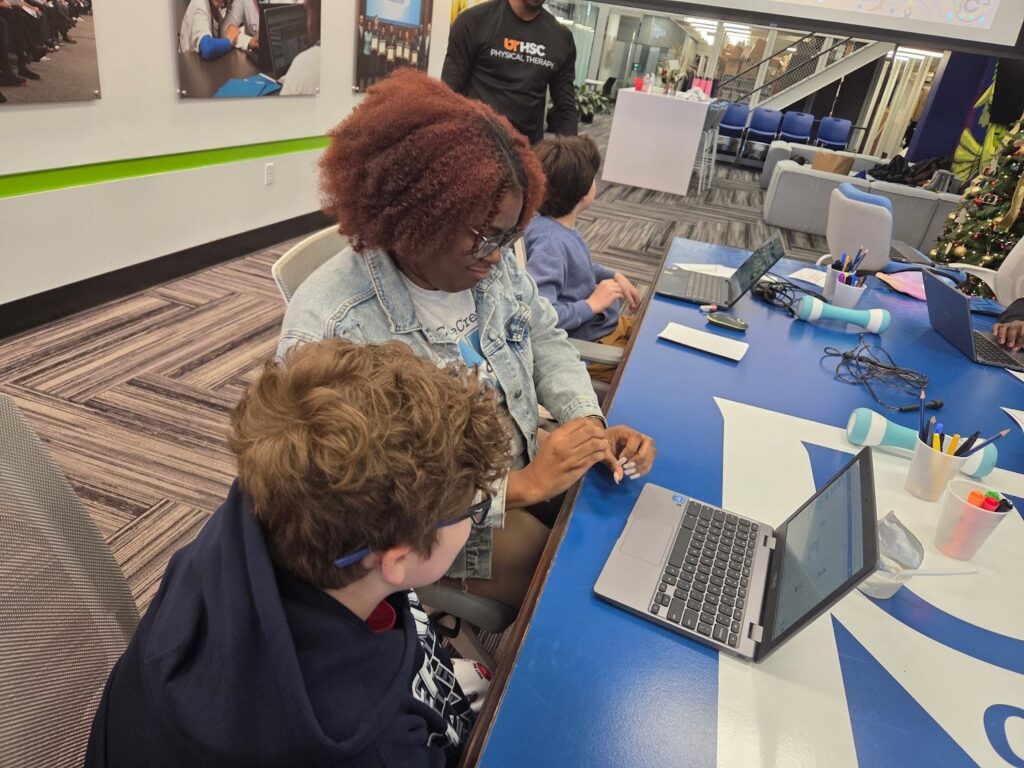 Two students working together on a laptop while a teacher walks around 