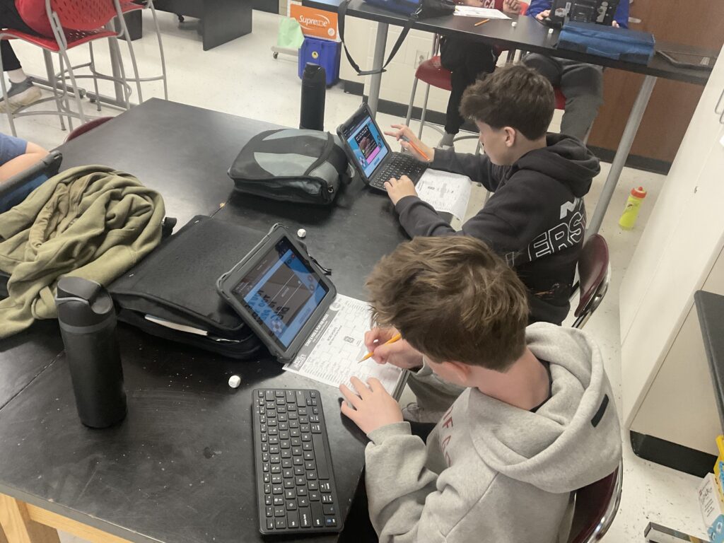 Two students working on a worksheet while completing a learning module on individual tablets